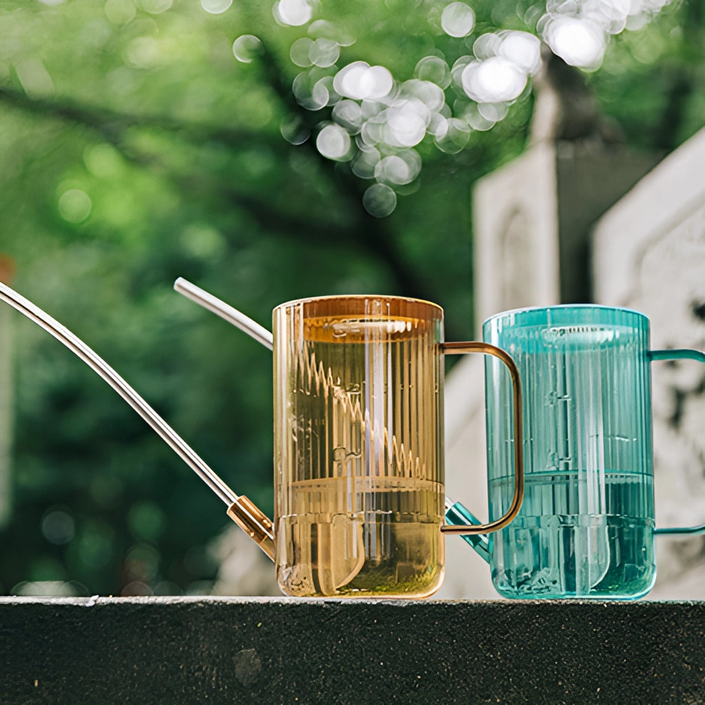 A blue watering can with an extended spout, placed on green grass.
