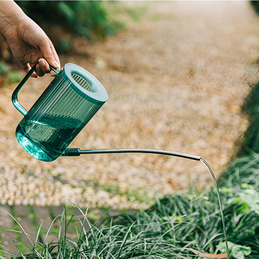 A green watering can with an extended spout for accurate water delivery, placed on a lush green lawn.