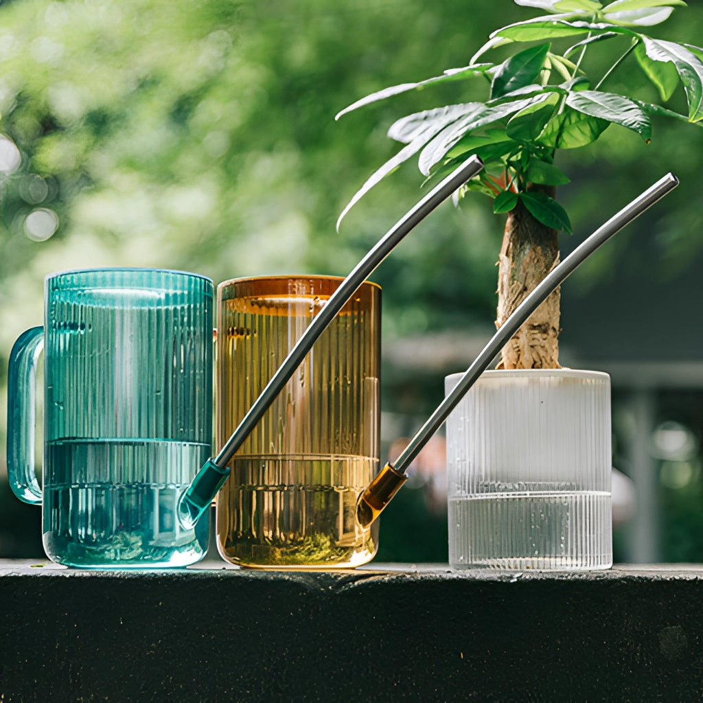 A watering can with an extended spout, designed for accurate water delivery, placed next to a green plant on a grassy surface.