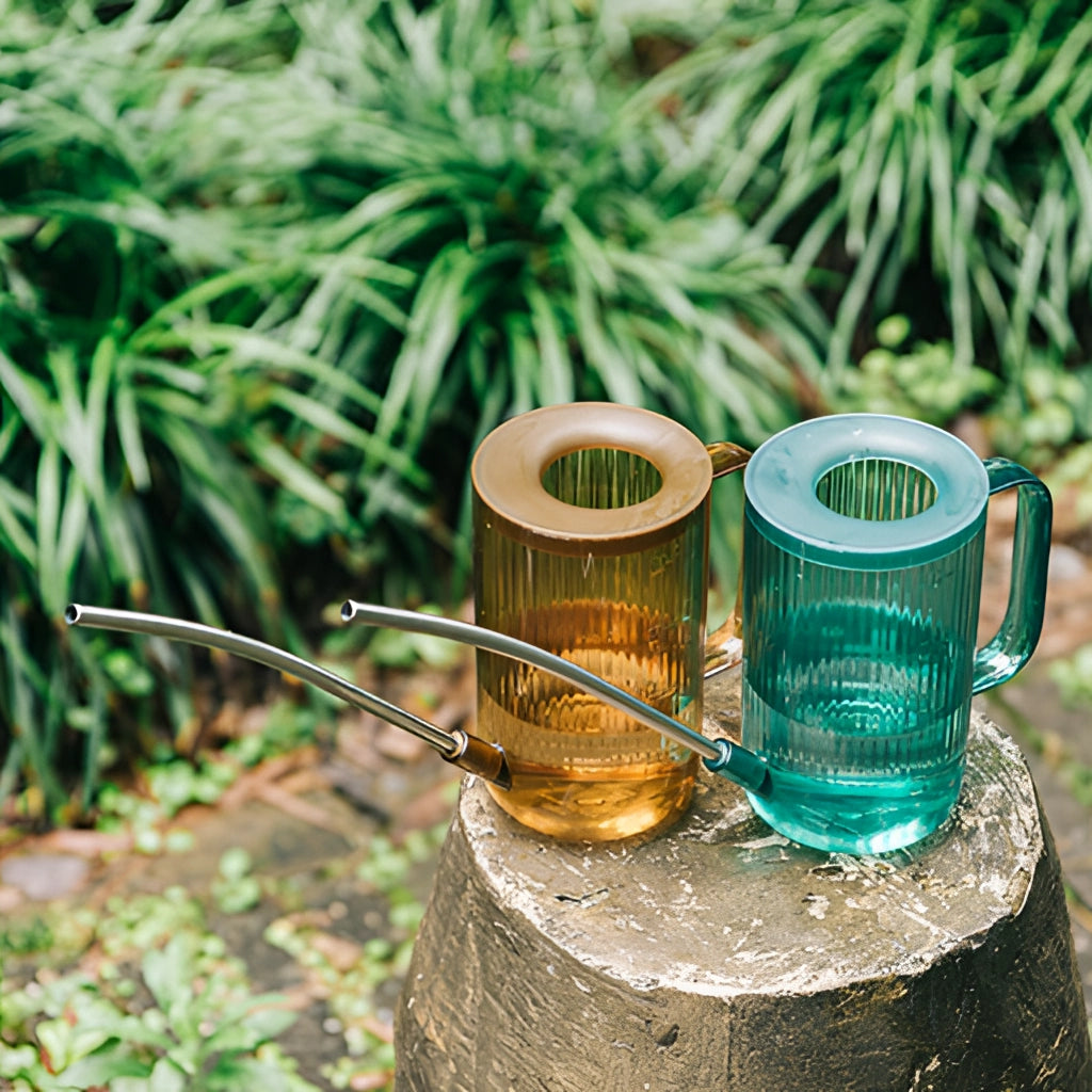 Watering can with extended spout placed on a wooden surface next to a plant.