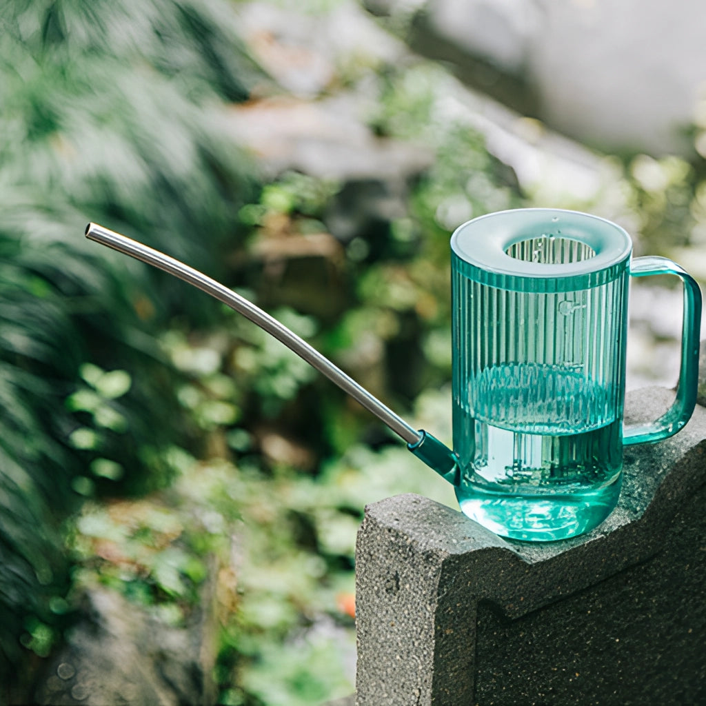 A blue watering can with an extended spout designed for accurate water delivery, positioned on a grassy surface.