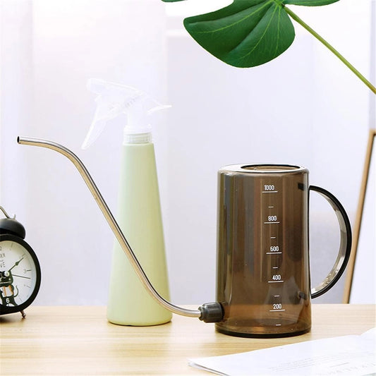 Watering tools set including a plastic watering can and spray bottle placed on a wooden table surrounded by green plants.