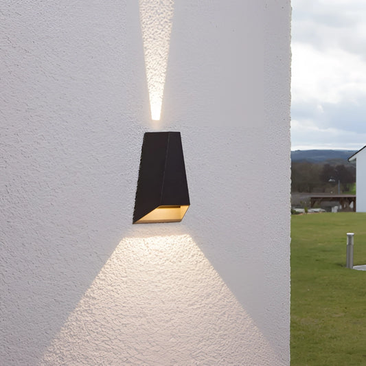 A waterproof outdoor pyramid LED wall sconce mounted on a concrete wall, surrounded by plants and illuminated against a twilight sky.