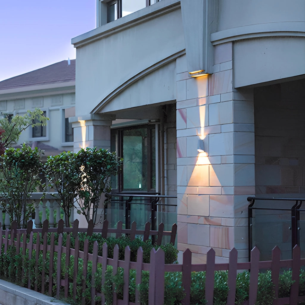 Waterproof Outdoor Pyramid LED Wall Sconce mounted on the exterior wall of a modern house near a window with plants and a fence visible nearby.