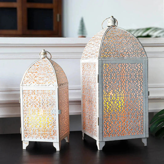 Set of 2 white gold metal candle lanterns displayed indoors on a wooden table near a window, perfect for indoor and outdoor decor.