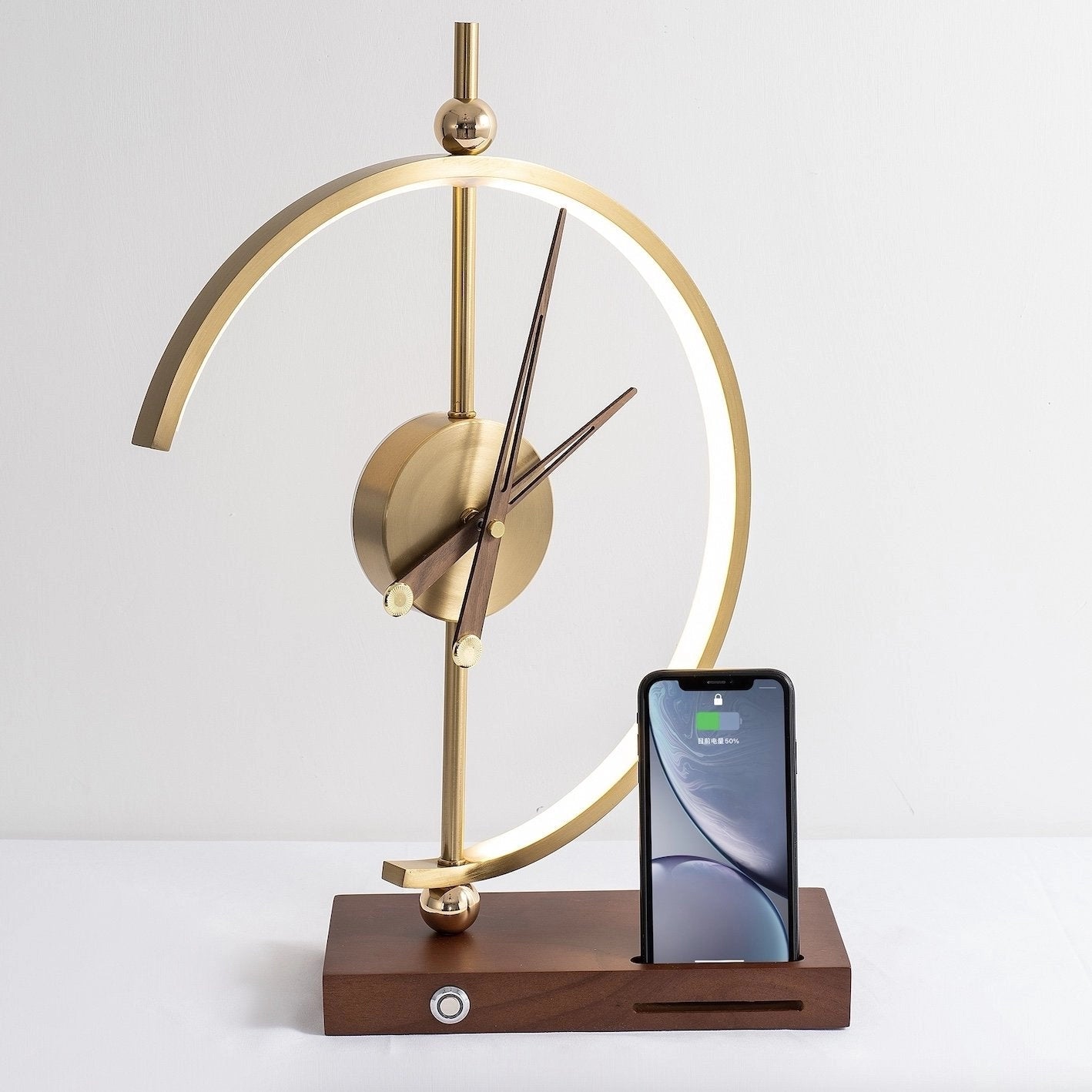 Wireless charging clock lamp with LED light, integrated clock, and wooden base, placed on a desk with a small plant nearby.