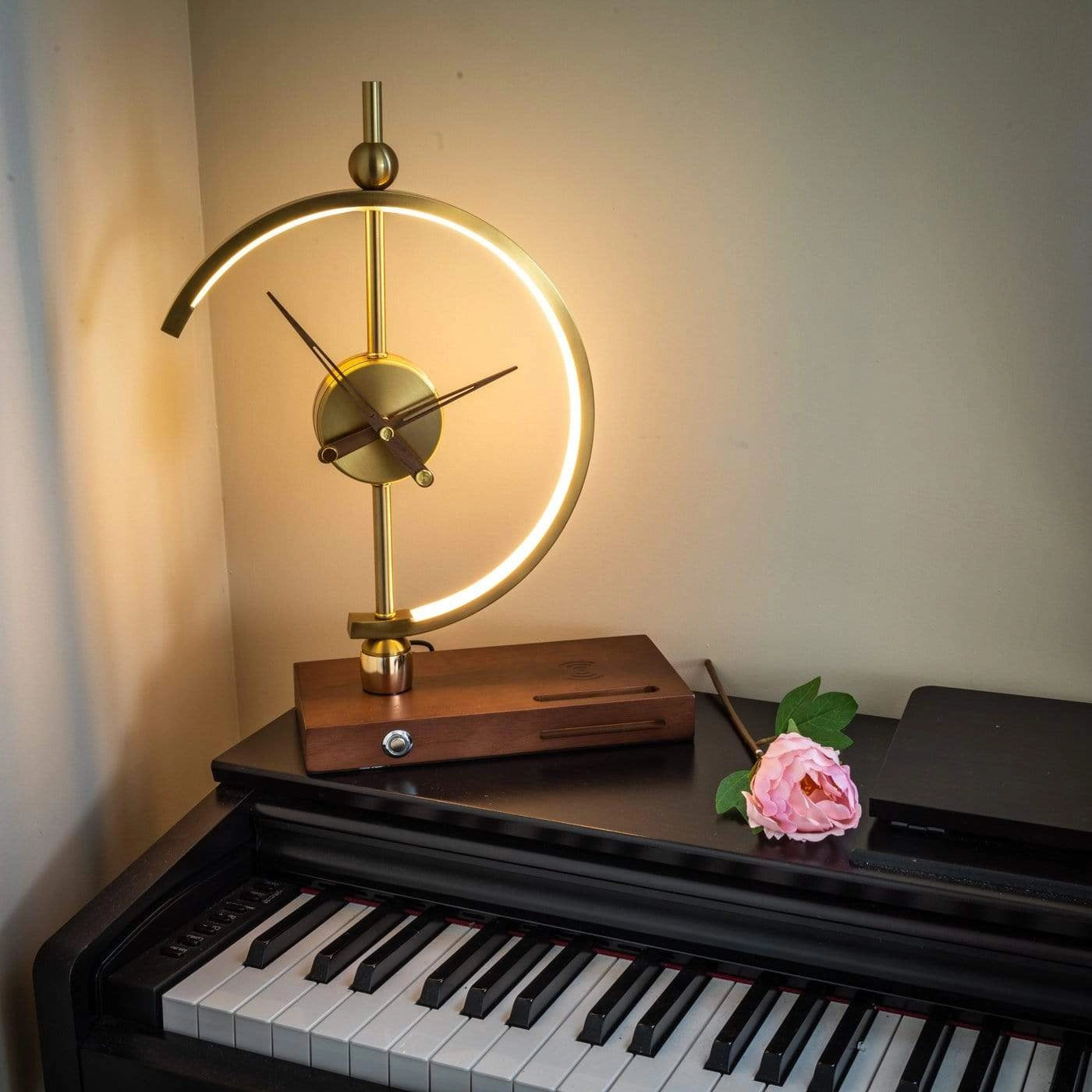 Wireless charging clock lamp with LED light and integrated clock on a wooden desk next to a keyboard piano.