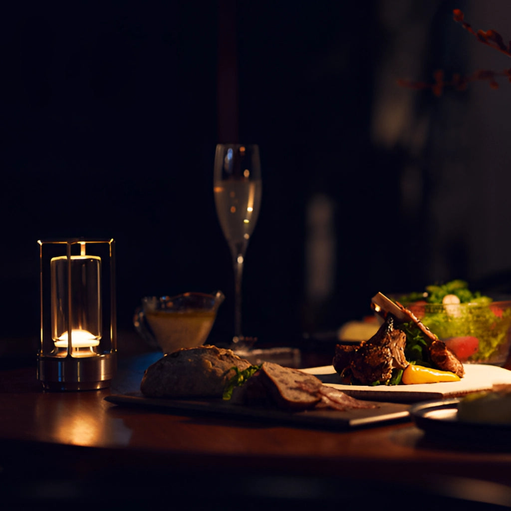 A wireless crystal lantern table lamp placed on a table along with tableware, including a plate and various drinkware like wine glasses and champagne stemware.
