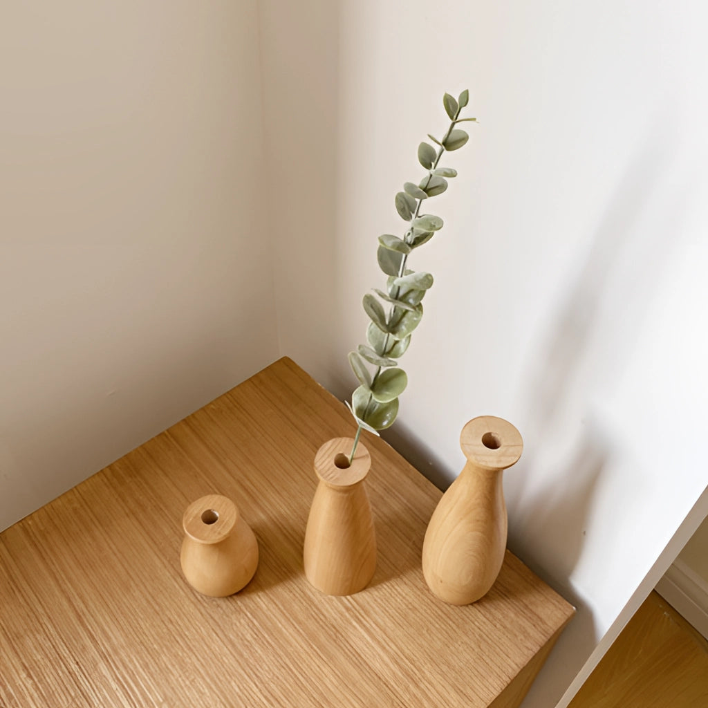 Tall wooden decor vase placed on a wooden floor next to a table, featuring a natural wood finish and holding decorative twigs.